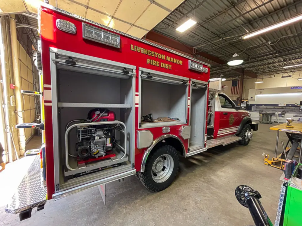 Exterior view of small fire truck showing cab, body compartments, and wheel/tire area.